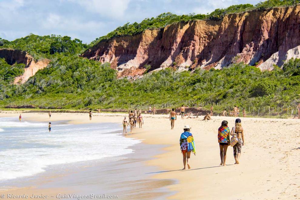 Imagem de pessoas caminhando próximo ao mar e ao fundo lindas falécias.